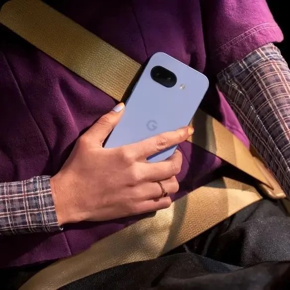 Pixel 9a in Iris colour being held in hand above purple jumper