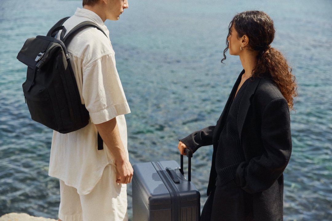 Man and woman standing by the sea wearing a travel backpack